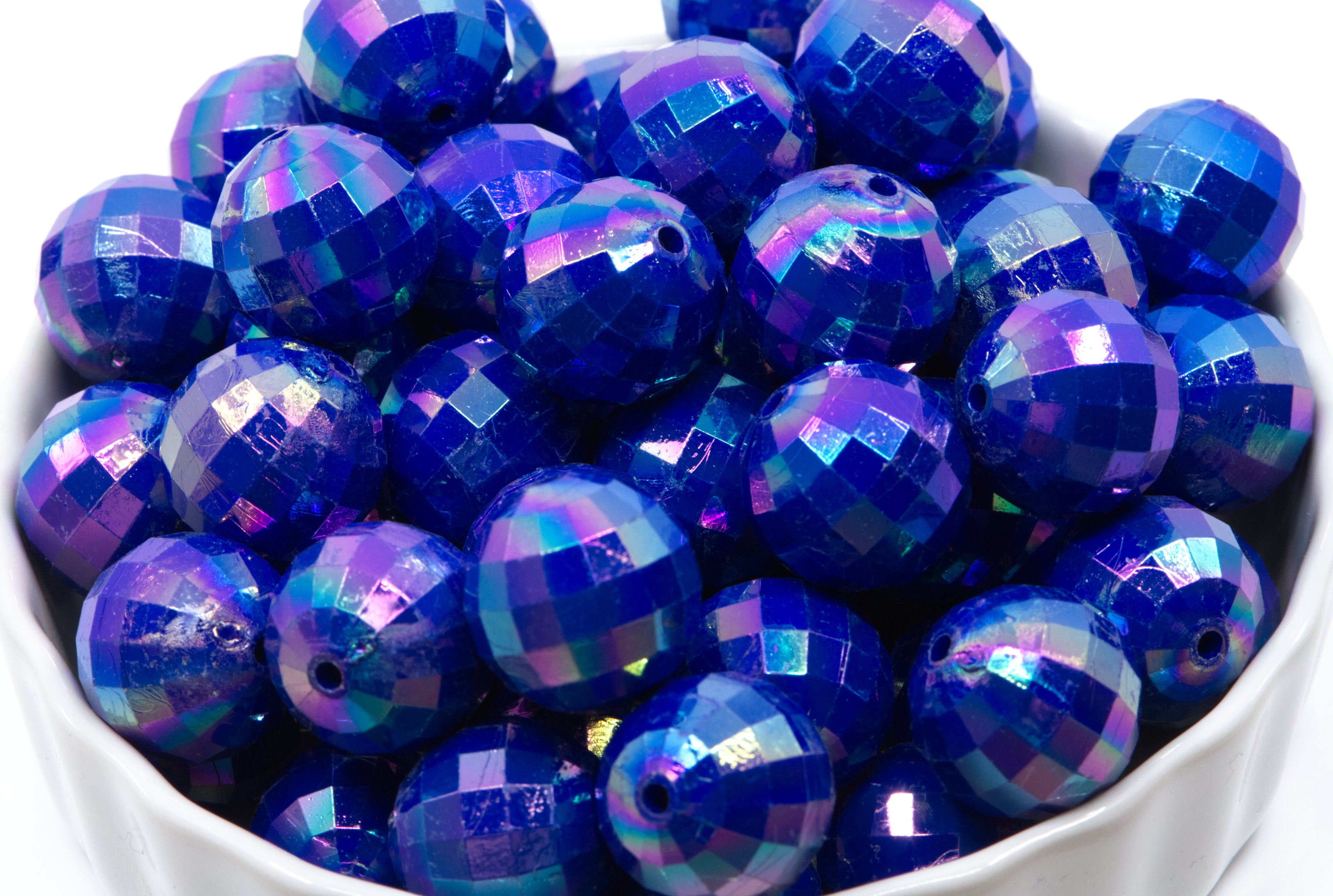 Blue faceted beads in a white bowl on a white background 