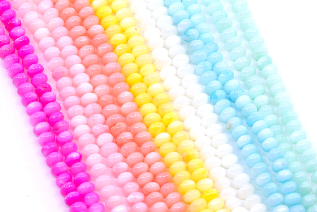 Multiple strands of abacus shell beads in bright colors, including pink, peach, yellow, white, and light blue, arranged diagonally on a white background.