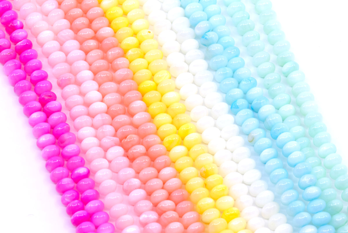 Multiple strands of abacus shell beads in bright colors, including pink, peach, yellow, white, and light blue, arranged diagonally on a white background.