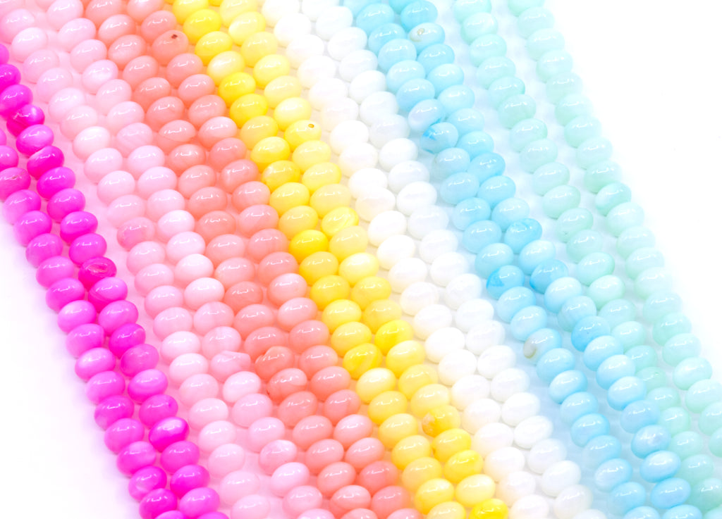 Multiple strands of abacus shell beads in bright colors, including pink, peach, yellow, white, and light blue, arranged diagonally on a white background.