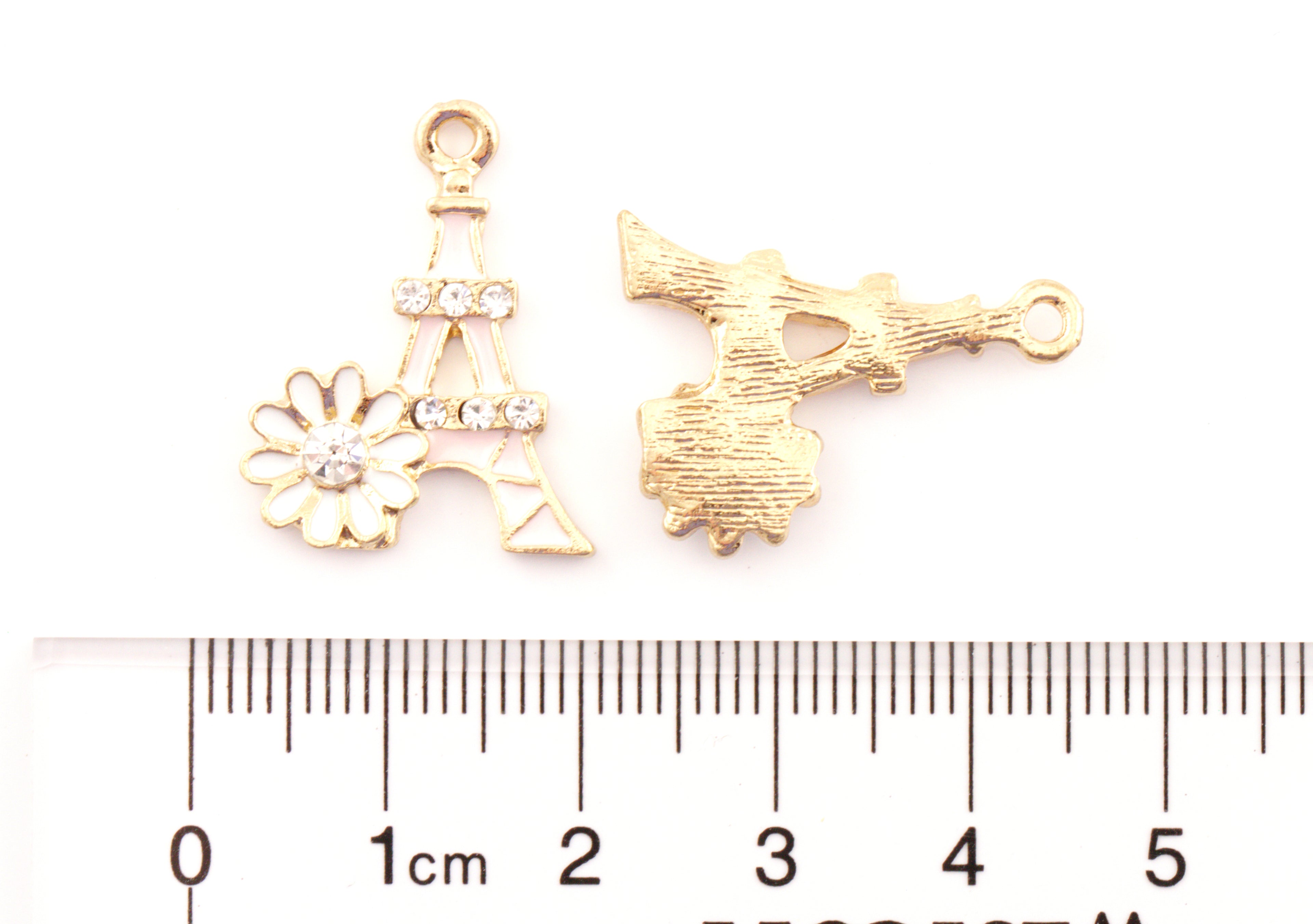Two pale pink Eiffel Tower  jewelry charms with a daisy and rhinestone detailing shown on a white background above a ruler for scale. 