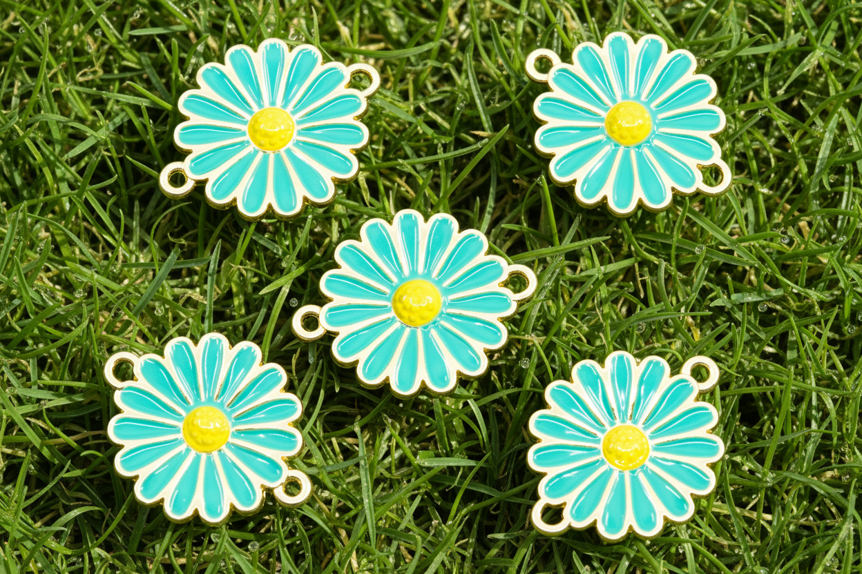 Five blue and yellow enamel flower charms with gold-tone metal edges and small hanging loops, arranged on green grass.