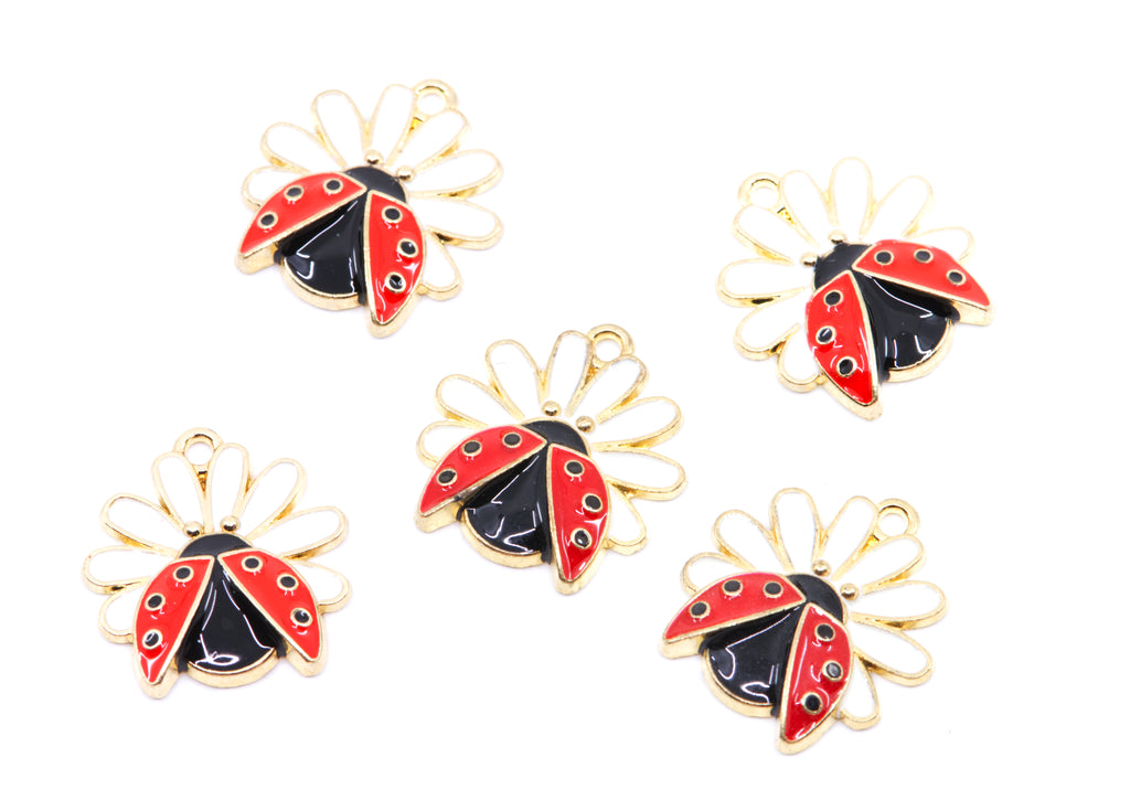 Five ladybug charms with gold-tone metal outlines, red and black enamel, and small white flower petals, arranged on a plain white background.