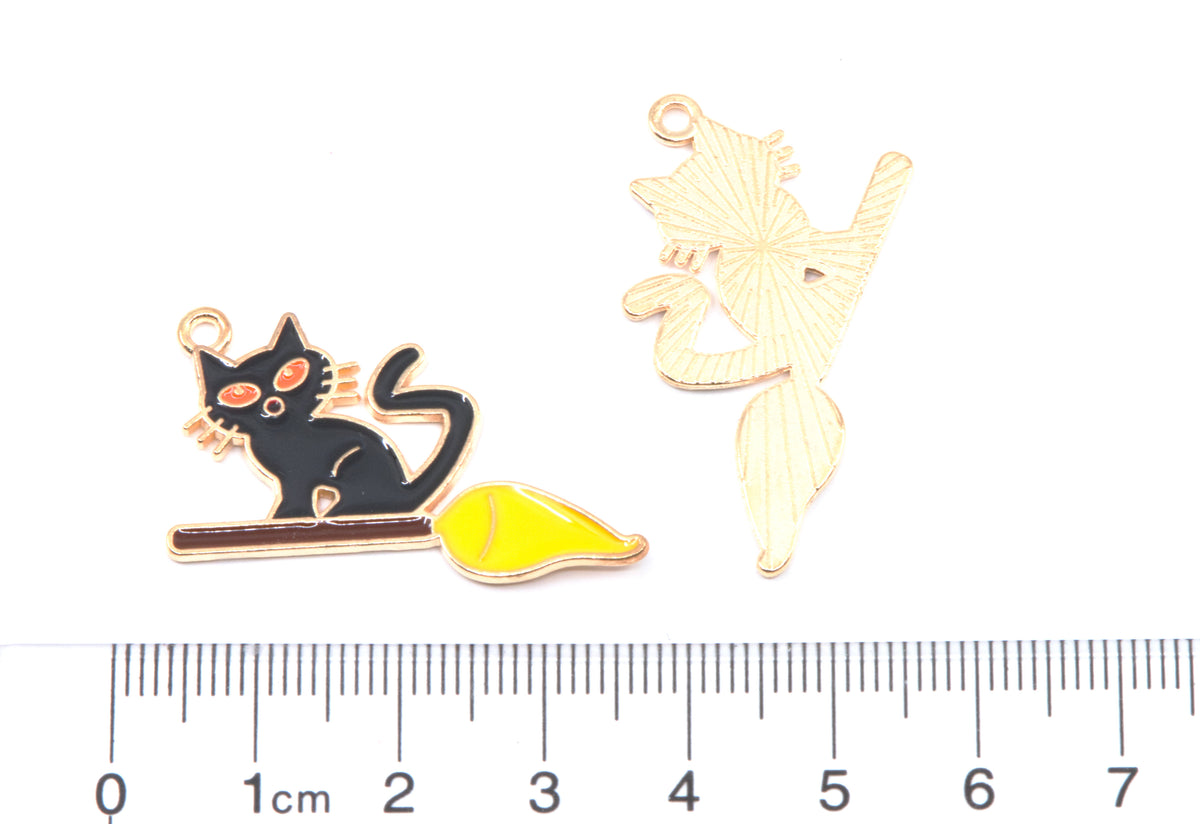 Two small jewelry charmsshown on a white background with a ruler at the bottom for scale. One charm is a black cat sitting on a branch with a yellow leaf and one is the same charm but shown as the back. 