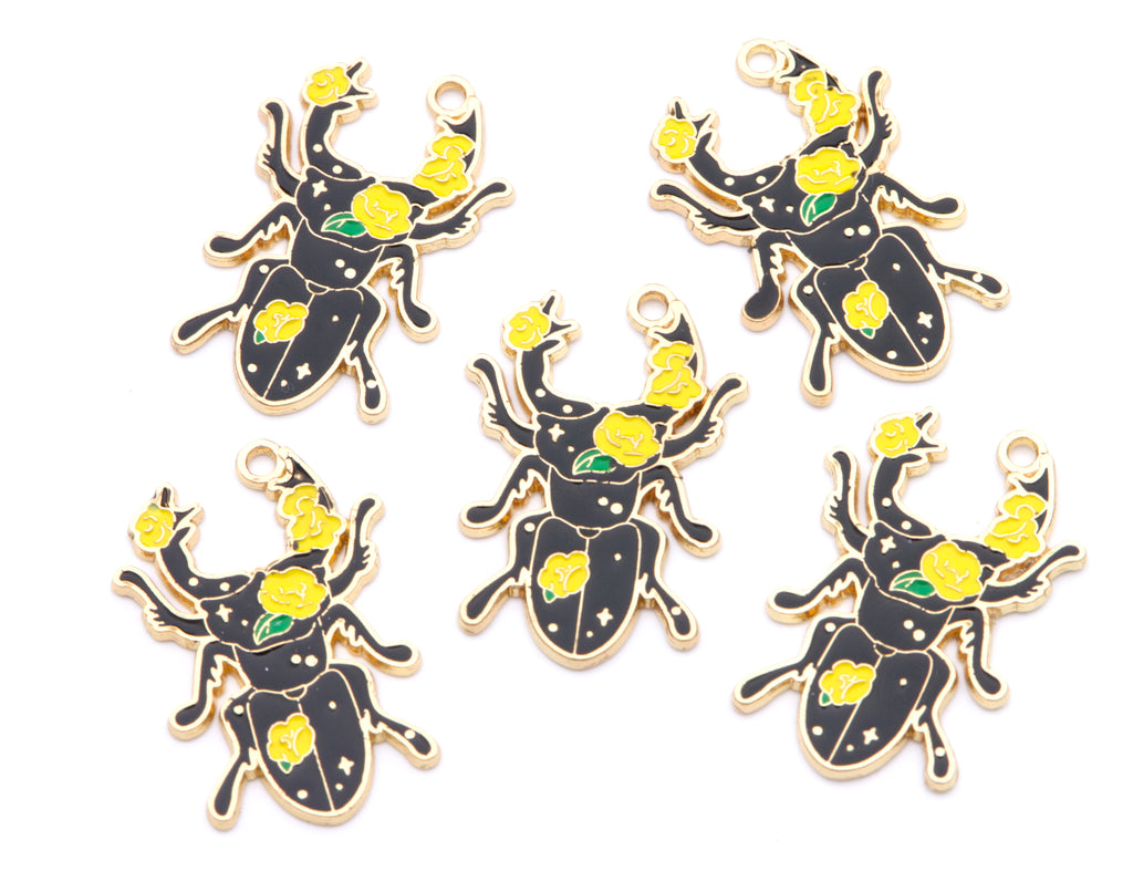 Five black beetle charms with gold-tone metal outlines, decorated with yellow roses and green leaves, arranged on a plain white background.