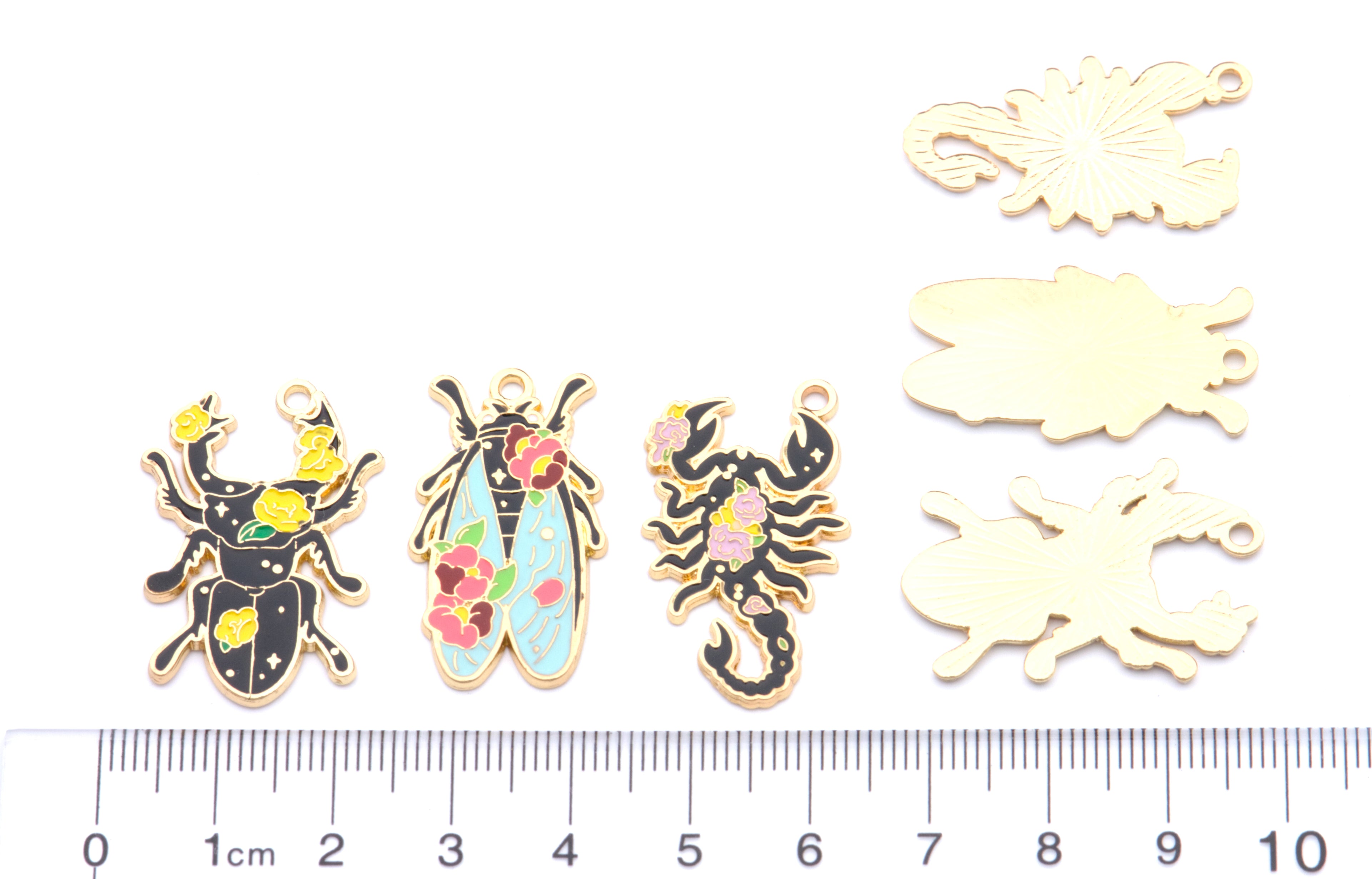 Six insect-shaped jewelry charms  displayed on a white background with a cm ruler at the bottom for scale. 