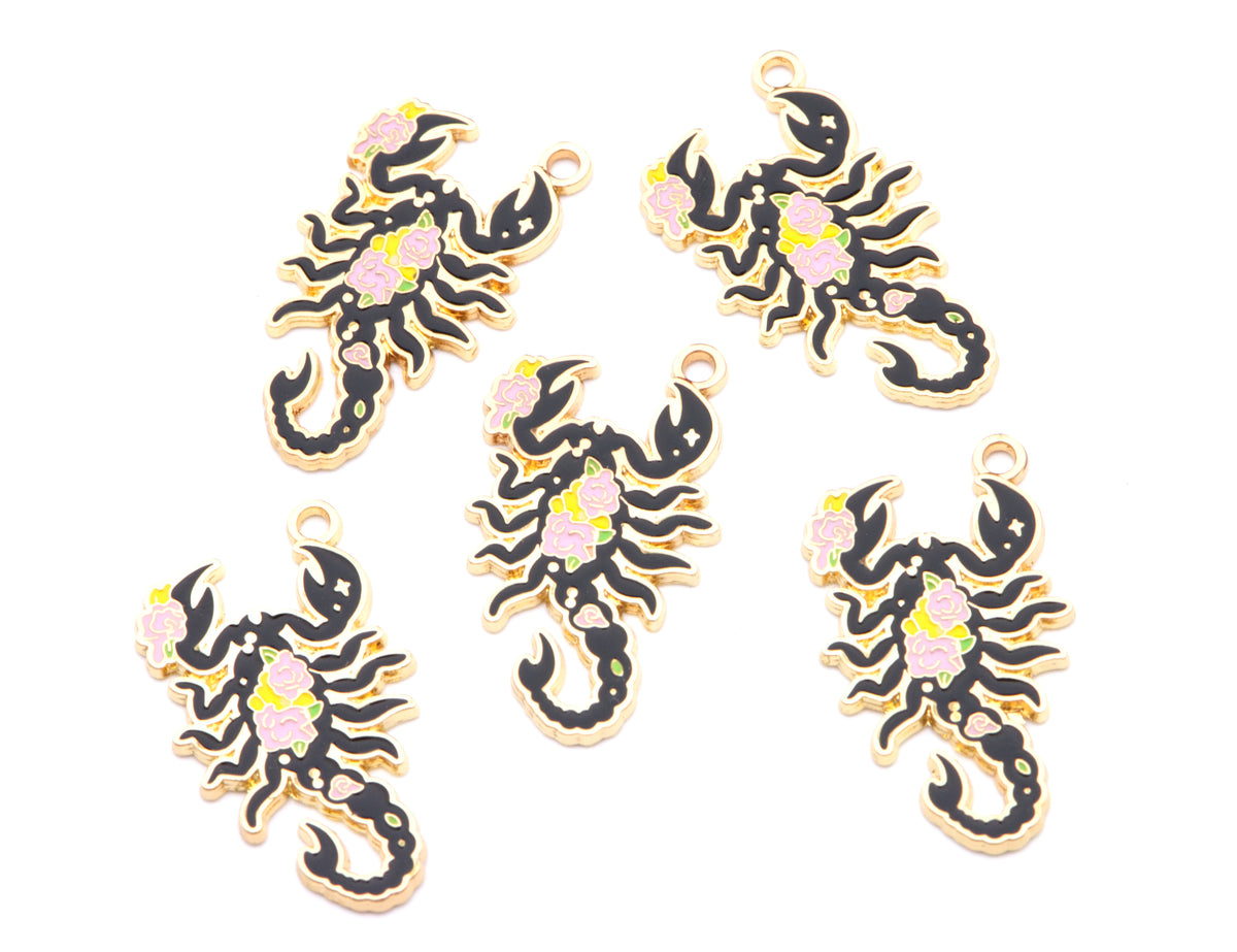 Five black scorpion charms with gold-tone edges and small pink and yellow floral accents, arranged on a plain white background.
