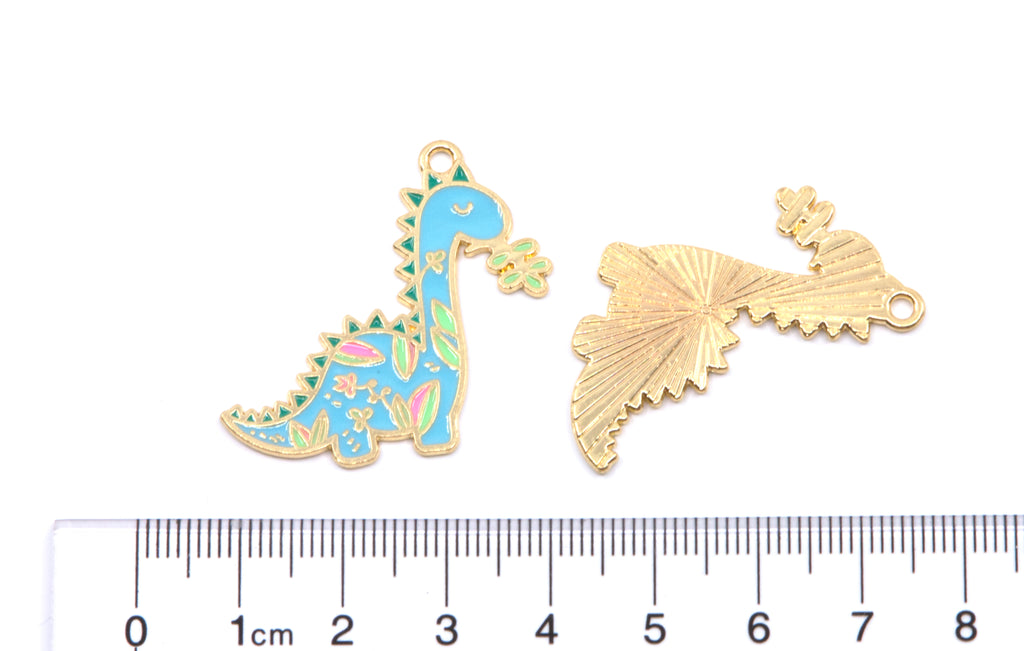 Two small jewelry charms shown on a white background with a ruler at the bottom for scale: one dinosaur charm in light blue enamel with multicolor floral details and gold-tone outline and he other is the back of the same charm