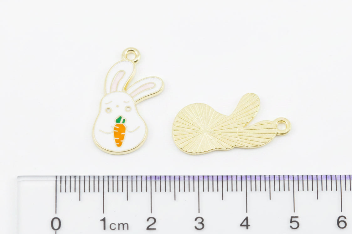 Two white bunny rabbit holding an orange carrot  jewelry charms placed above a ruler on a white background: