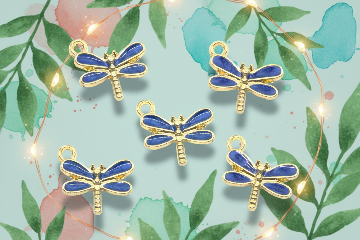 Five dragonfly charms with blue enamel wings and gold-tone bodies, arranged on a light blue background with watercolor leaves and warm string lights.