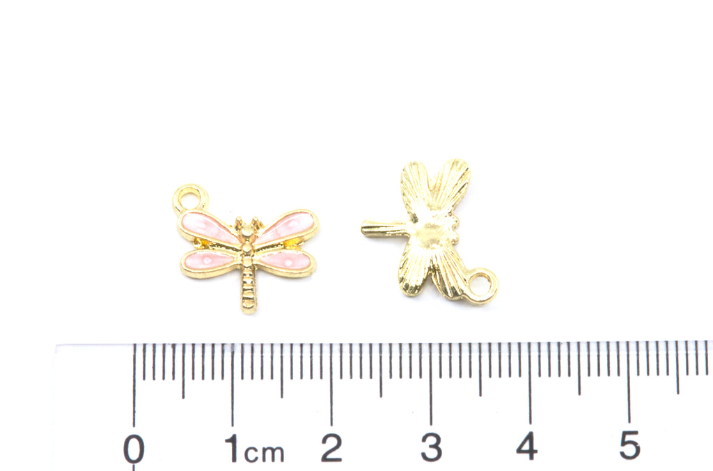 Two small dragonfly jewelry charms, one showing the front with pink enamel wings and the other showing the back with a loop, displayed above a cm ruler on a white background.