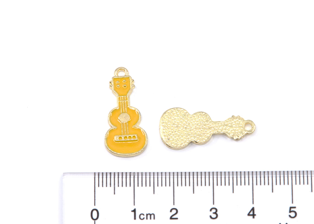 Two small guitar-shaped jewelry charms in gold-tone metal shown above a cm ruler for scale on a white background.