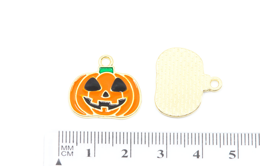 two orange jack o lantern enamel charms  on a white background with a cm ruler for scale.