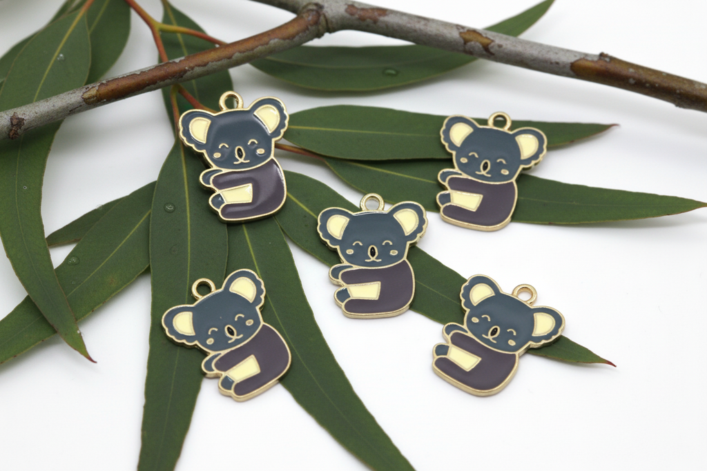 five gray koala charms shown on eucalyptus leaves on a white background 