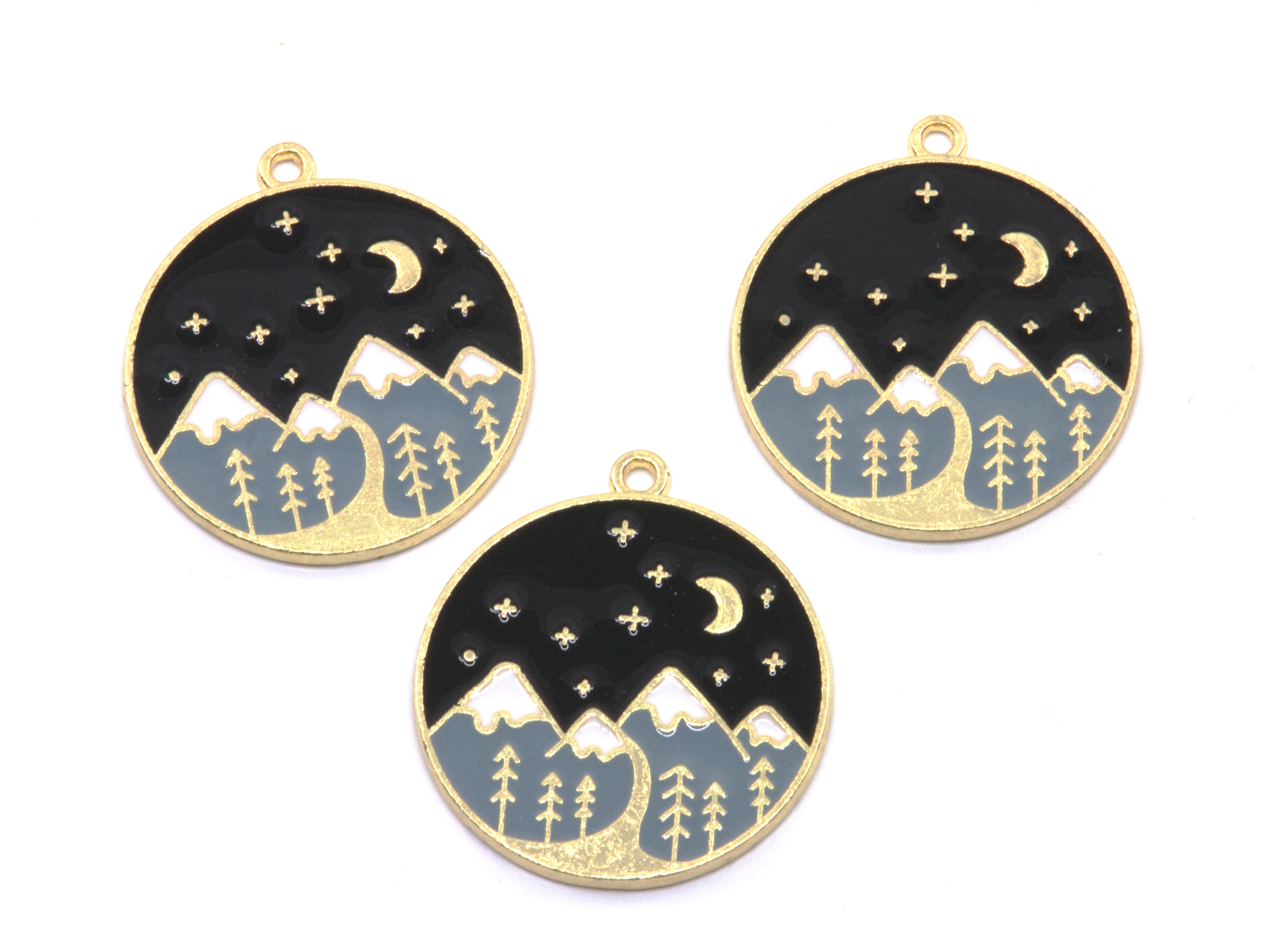 Three round gold-tone charms featuring a night sky and mountain landscape design, displayed on a clean white background.