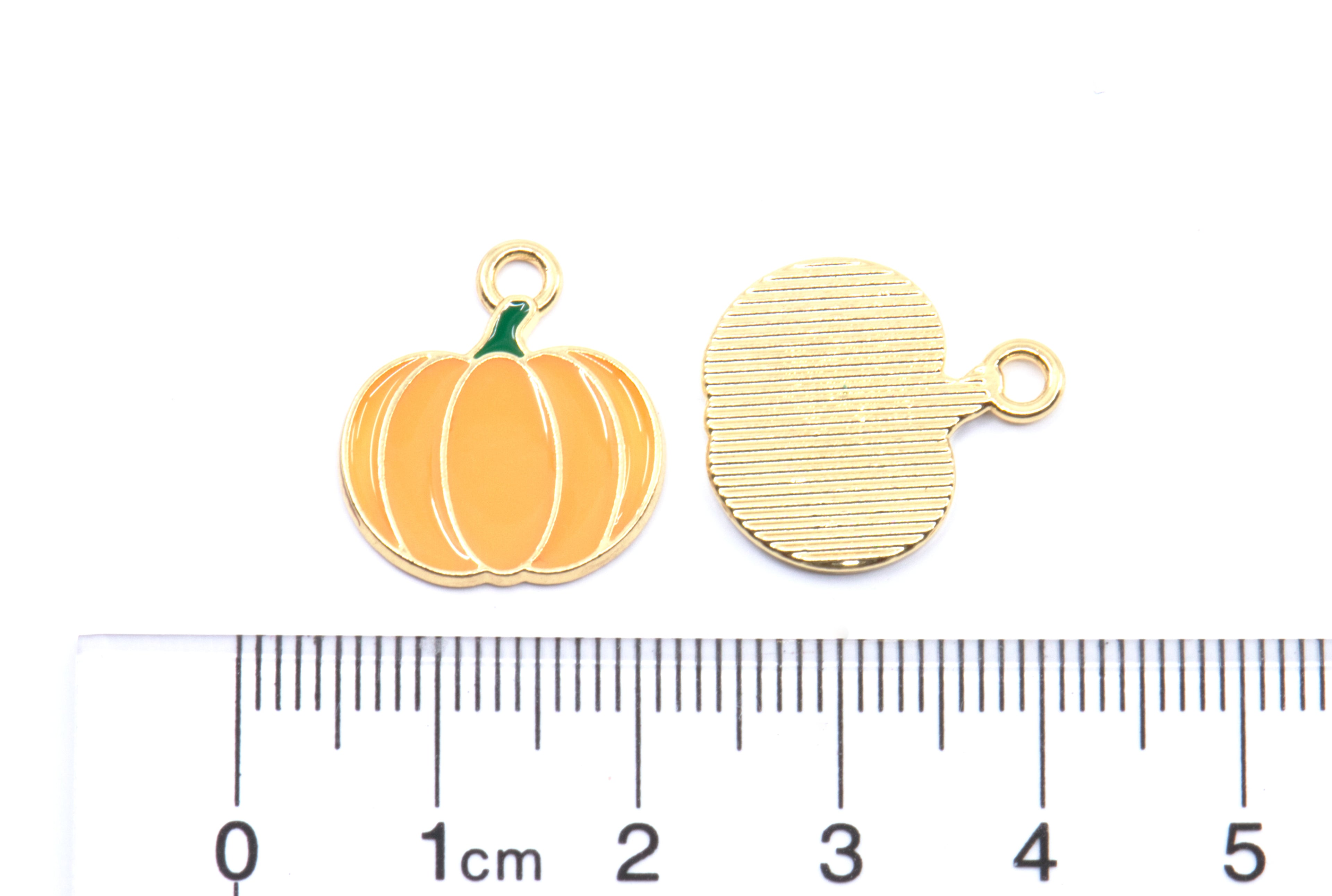 Two small pumpkin-shaped jewelry charms shown on a white background above a ruler for scale. 