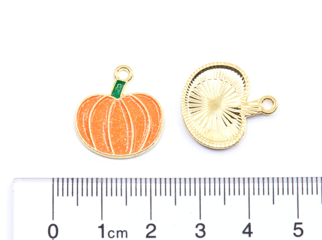 Two small pumpkin jewelry charms shown on a white background with a ruler at the bottom for scale. 