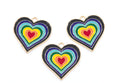 Three heart-shaped enamel jewelry charms with concentric rainbow heart designs and gold-tone borders, arranged on a plain white background.