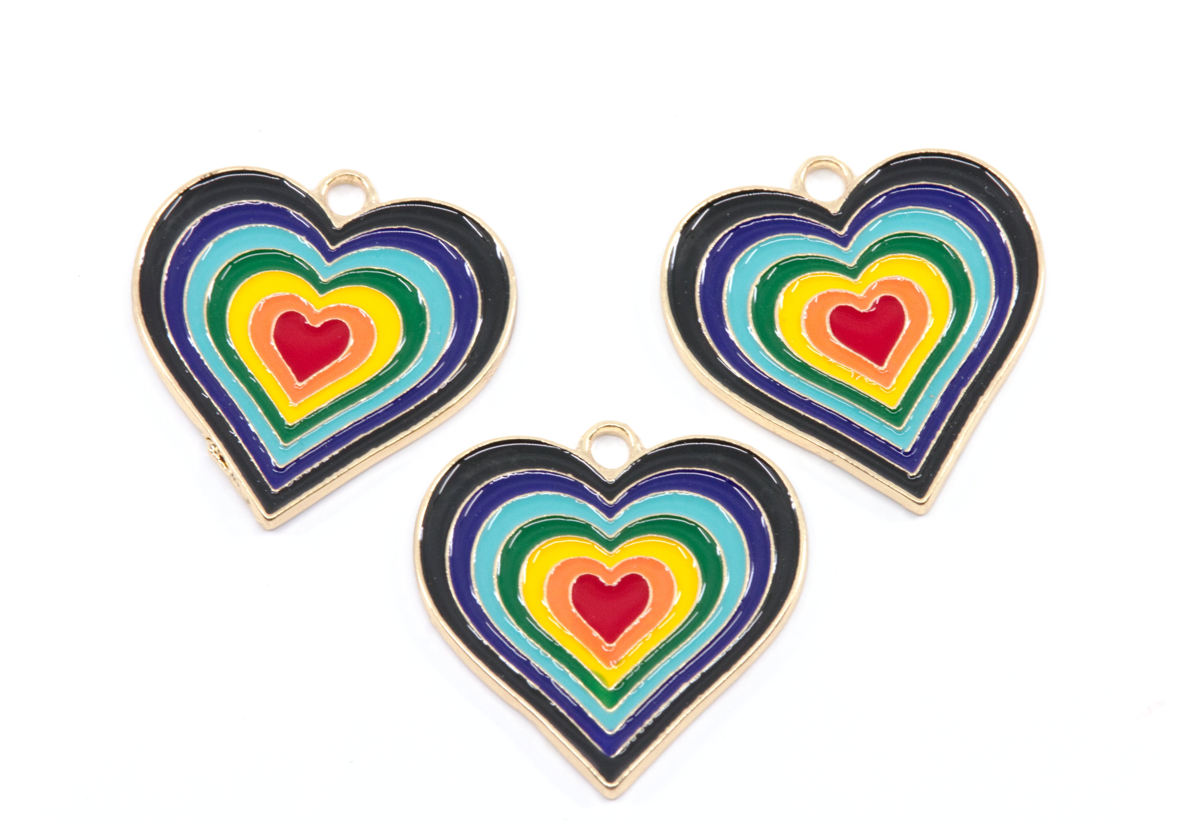 Three heart-shaped enamel jewelry charms with concentric rainbow heart designs and gold-tone borders, arranged on a plain white background.