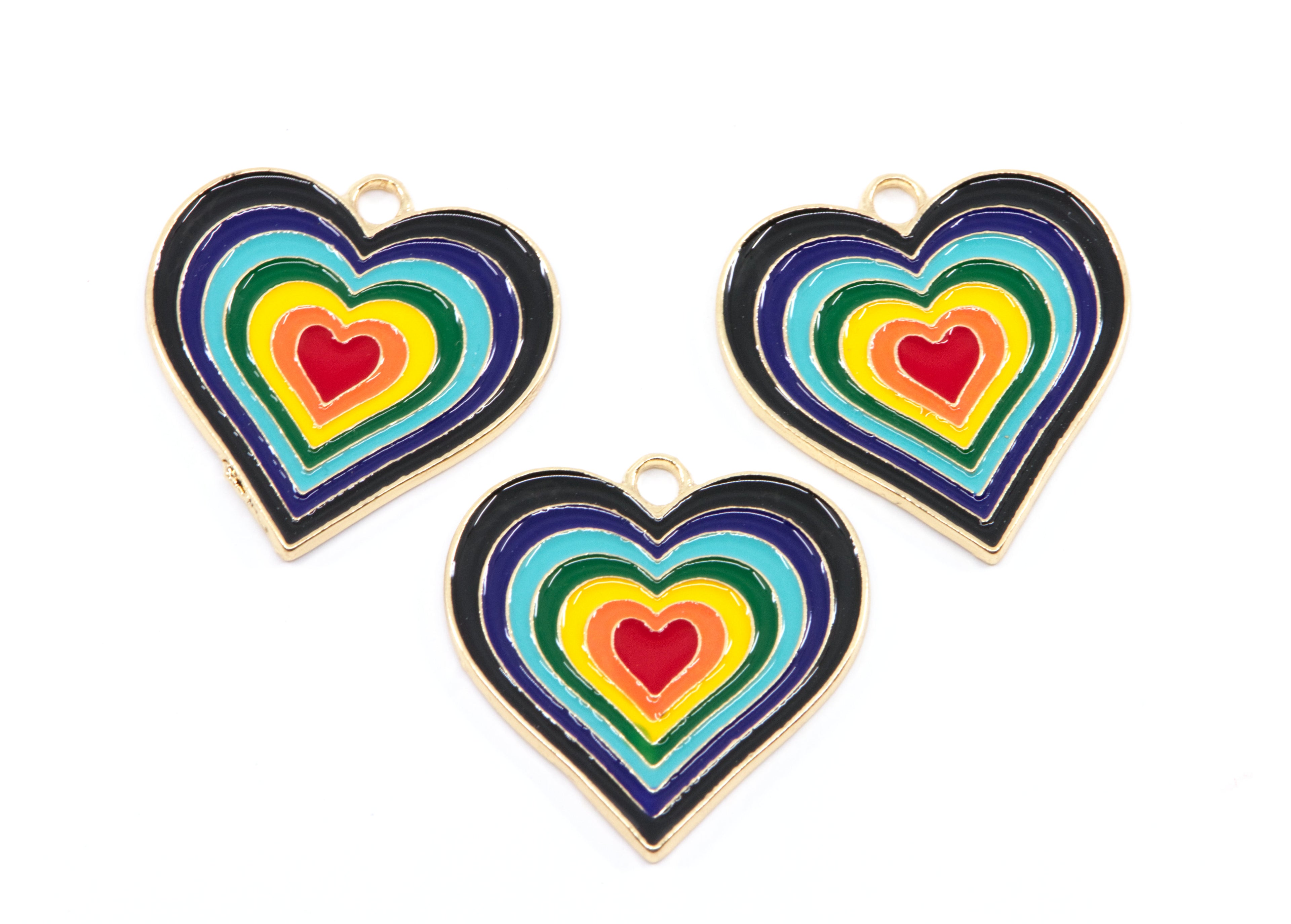 Three heart-shaped enamel jewelry charms with concentric rainbow heart designs and gold-tone borders, arranged on a plain white background.