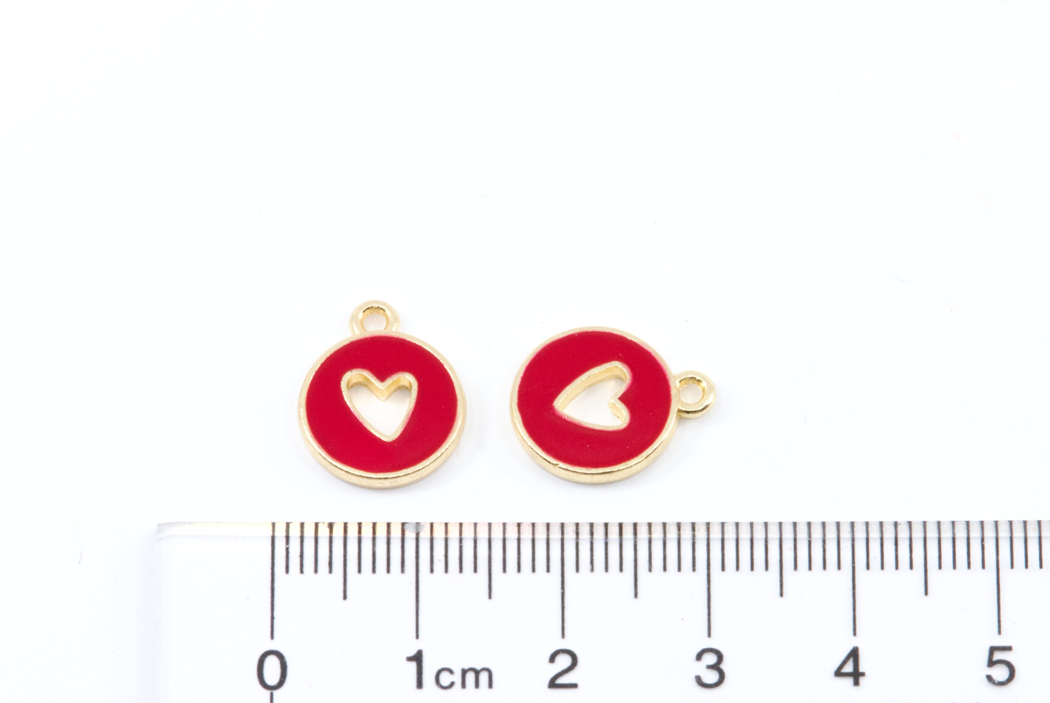 Two small round red and gold jewelry charms with heart cutouts, shown next to a cm ruler for scale on a white background.