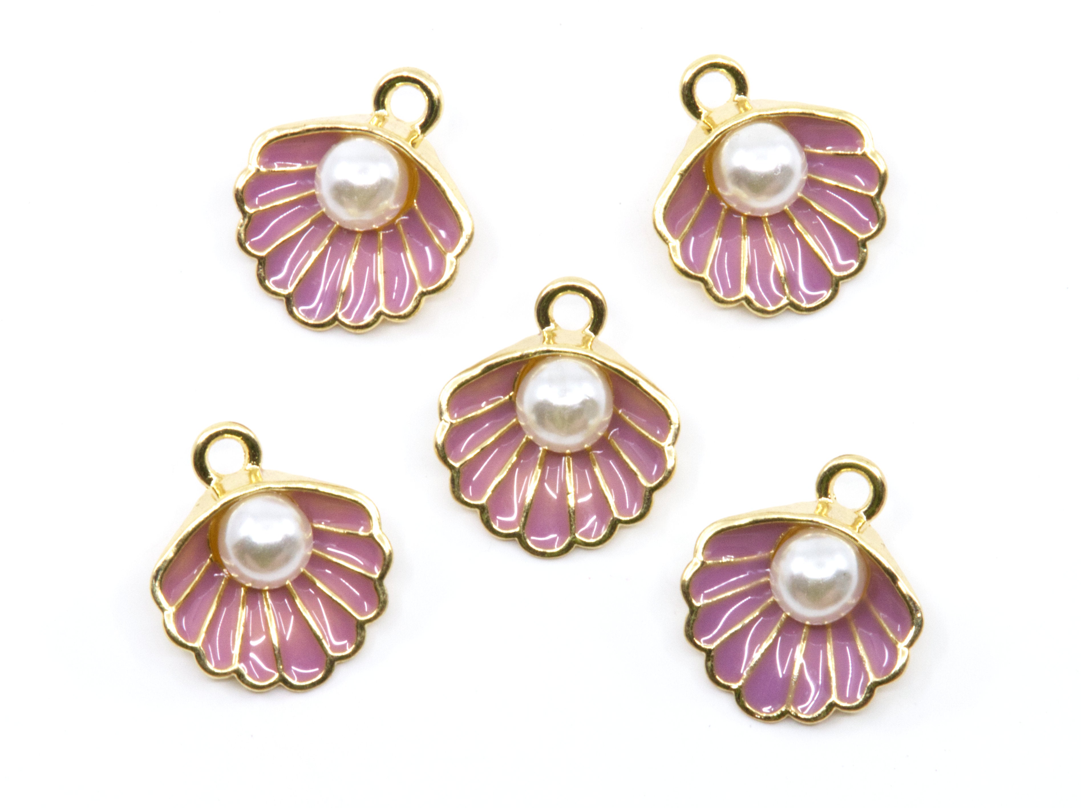 Five seashell-shaped jewelry charms with gold-tone metal edges, purple enamel detailing, and a white faux pearl in the center, arranged on a plain white background.