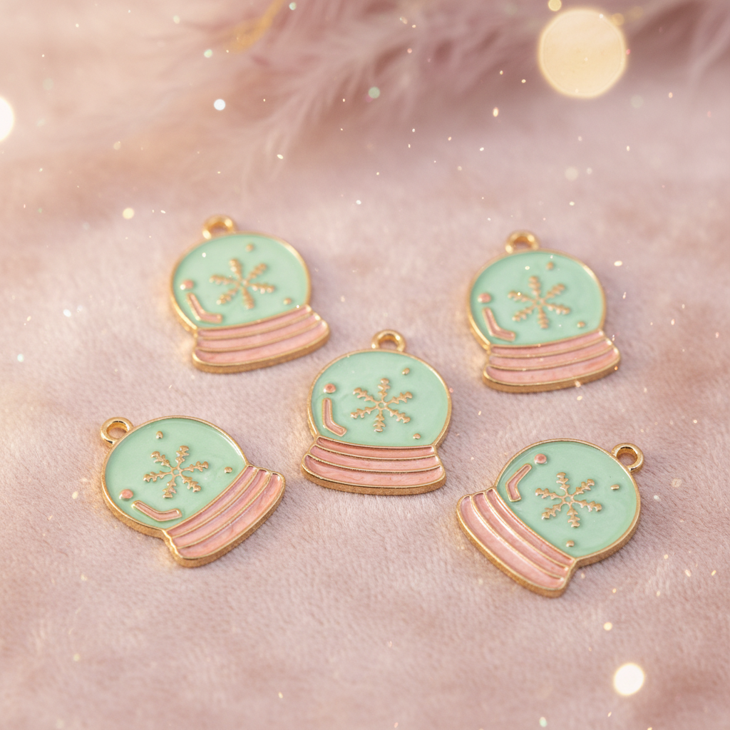Five blue and pink snow globe charms with gold-tone metal trim, arranged on a soft pink textured background with a glittery bokeh effect.