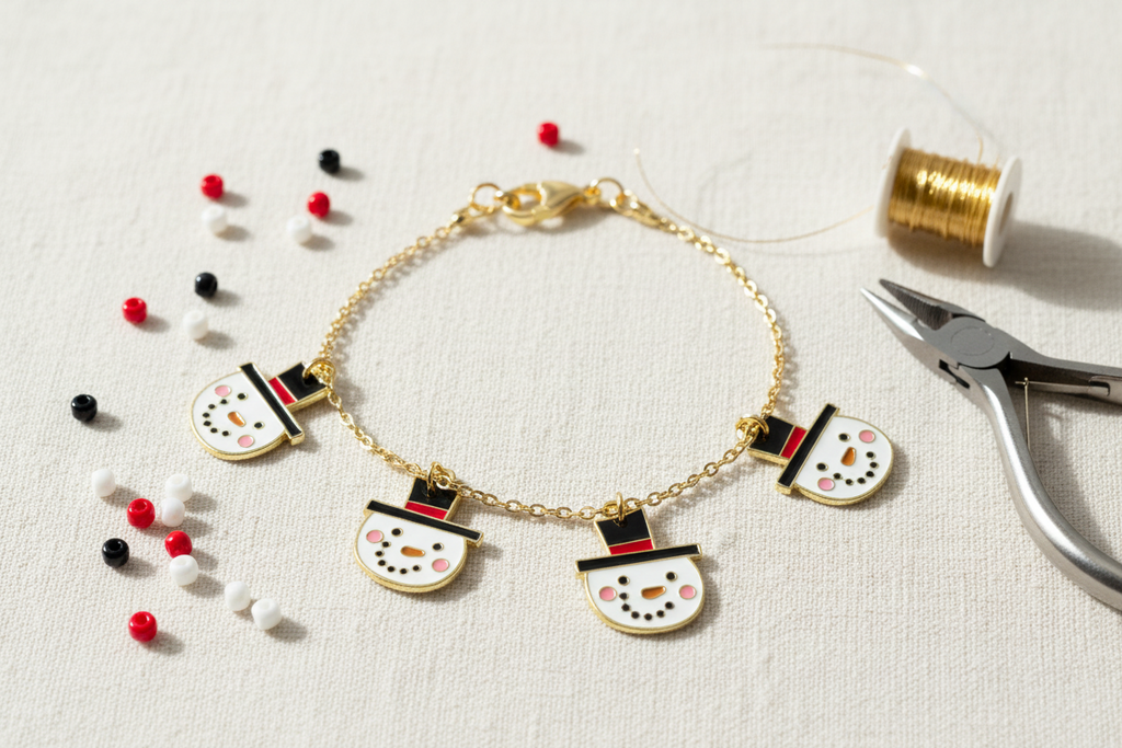 A gold chain bracelet with four snowman charms, styled on a textured white fabric background with sewing tools and beads nearby.