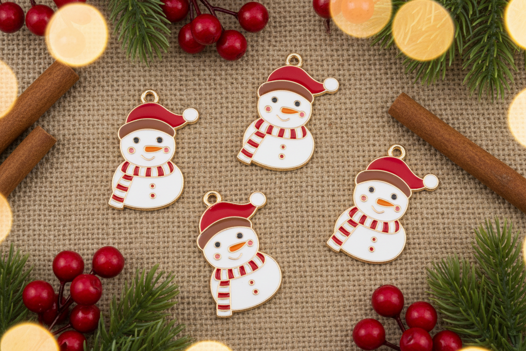Four white snowman Christmas ornaments with red hats and scarves, arranged on a burlap surface with pine branches, red berries, cinnamon sticks, and warm bokeh lights.