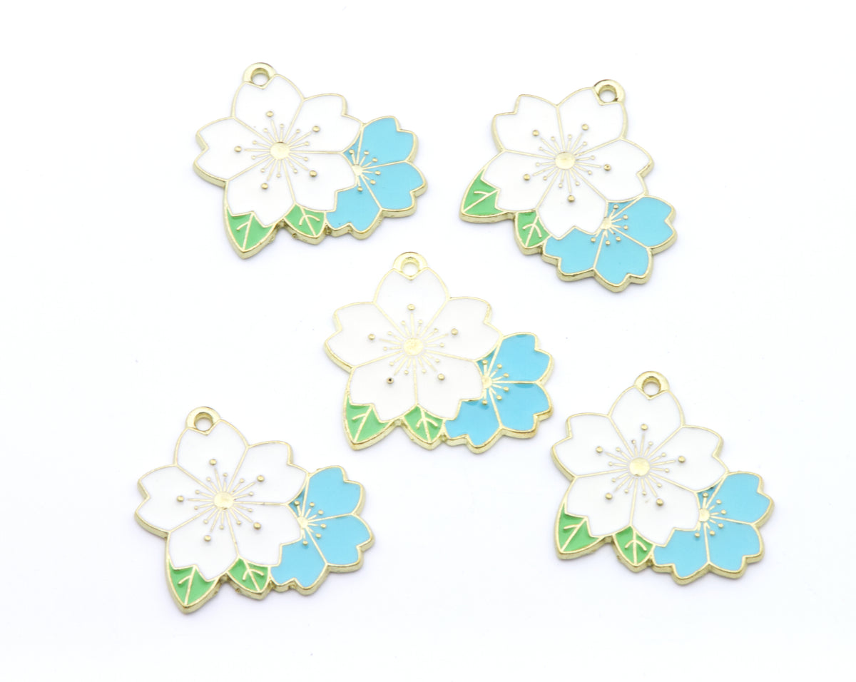 Five flower charms with white petals, light blue accents, and green leaves, outlined in gold metal, arranged on a plain white background.