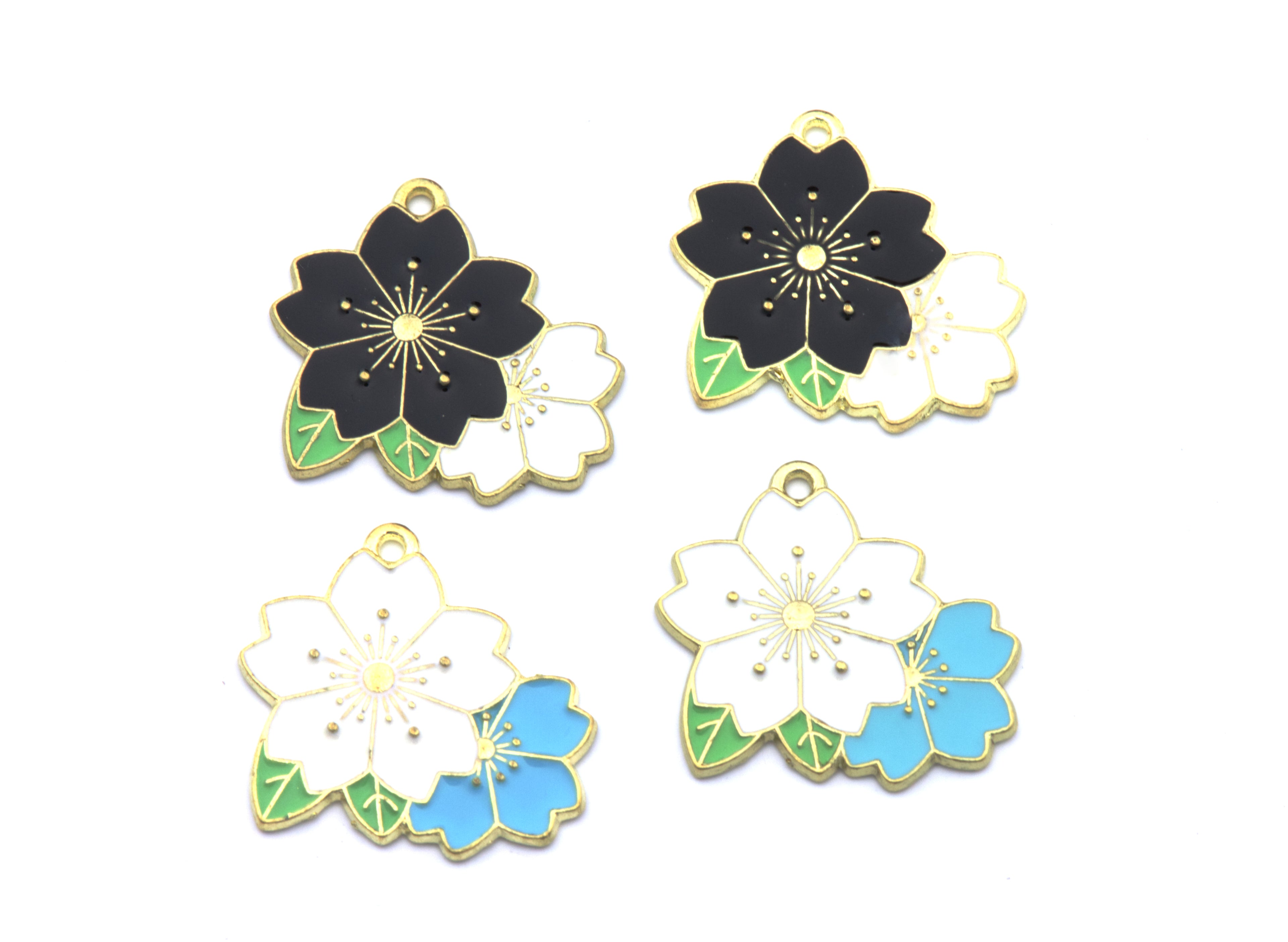 Four flower enamel charms with gold-plated edges, arranged on a plain white background. The charms feature black, white, and light blue flower designs with green leaves.
