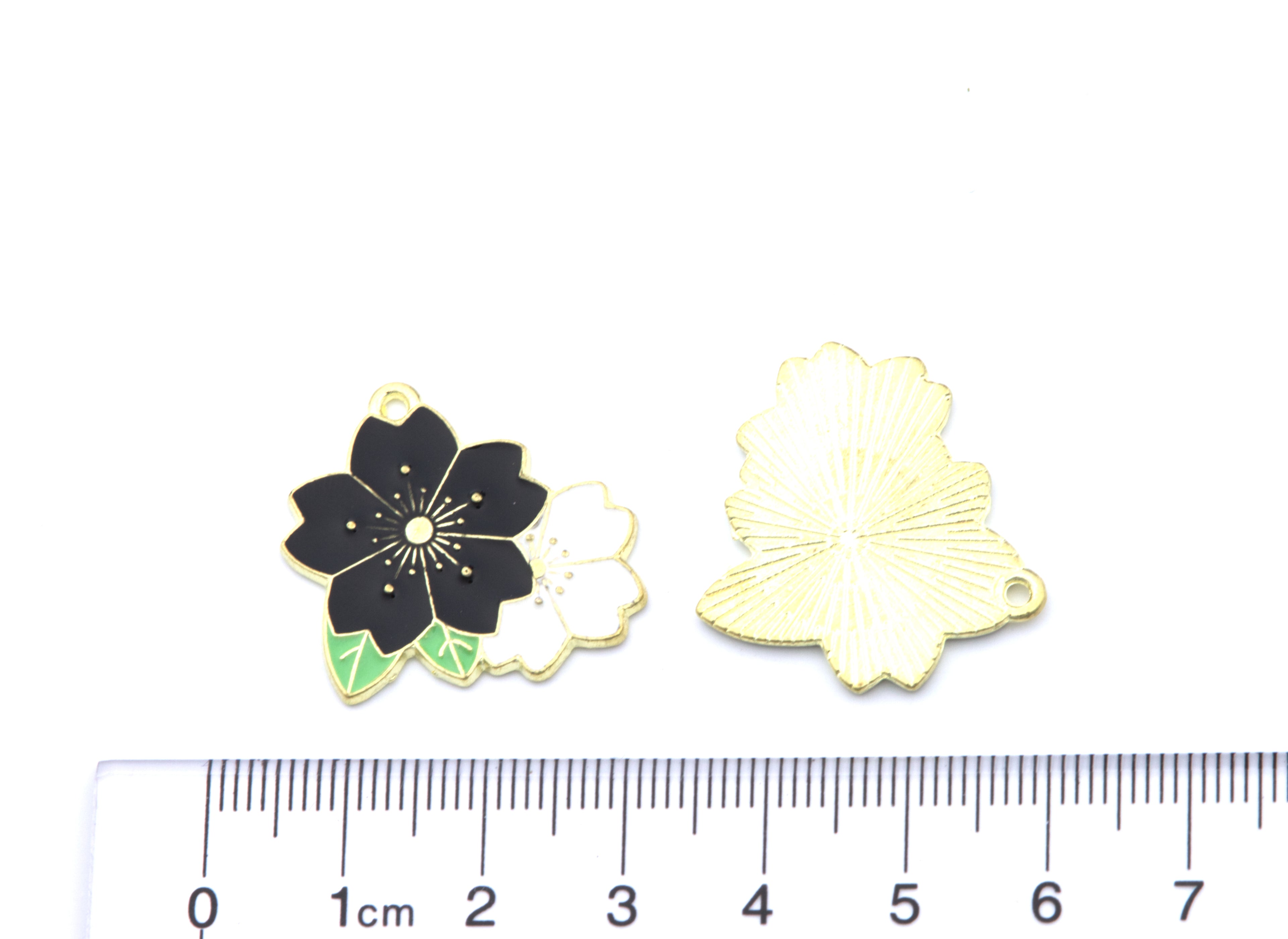 two black and white flower charms white background with a cm ruler for scale. 