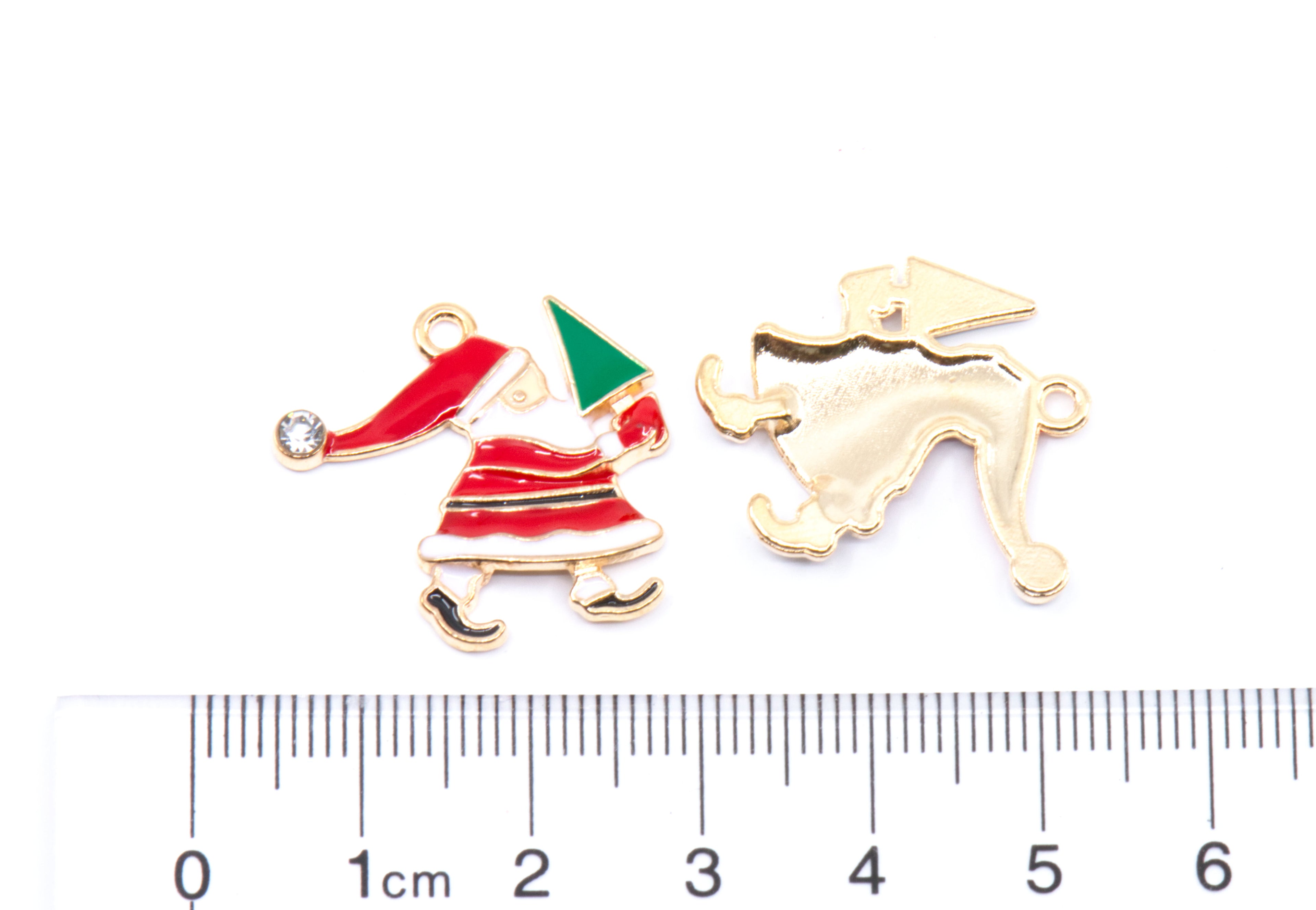 Two Red and white Santa carrying a green tree Christmas-themed charms shown on a white background with a cm ruler below for scale. 