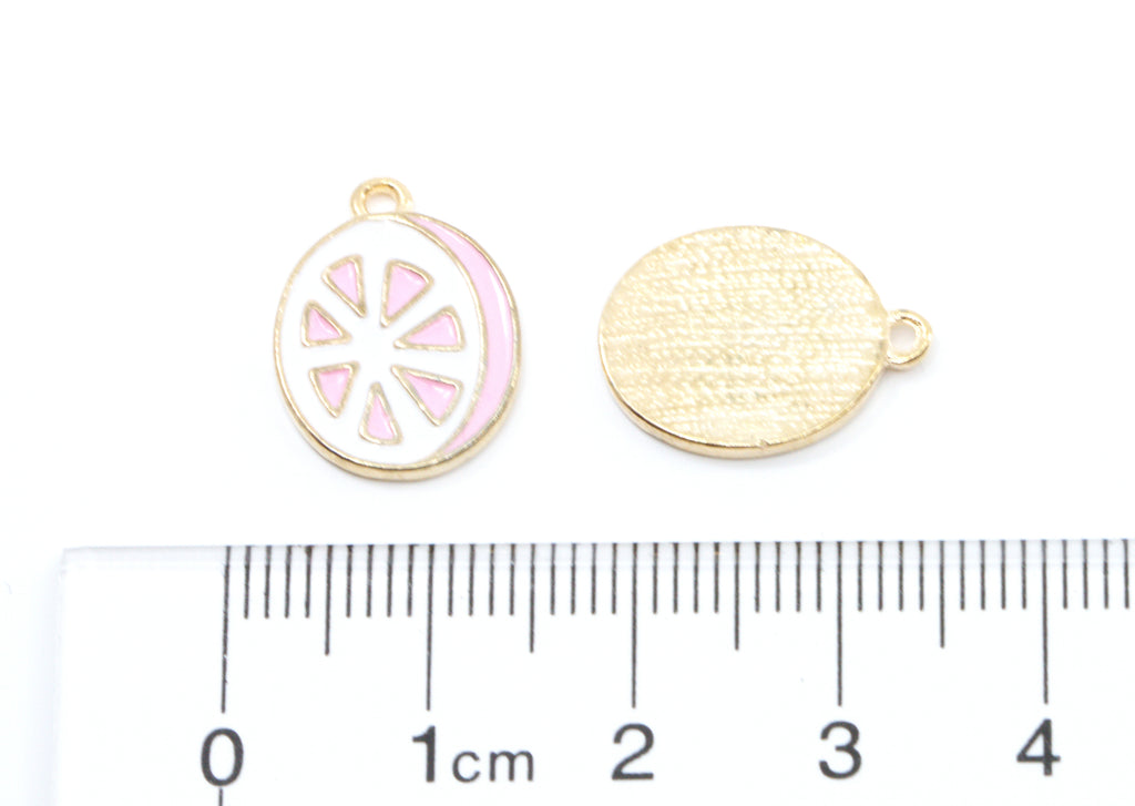 Two pink and white grapefruit slice jewelry charms shown on a white background with a ruler at the bottom for scale. 