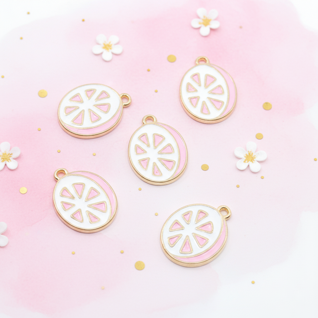 Five grapefruit slice enamel charms, featuring white centers with pink segments and gold-tone borders, arranged on a soft pink background with small white flowers and gold dots.