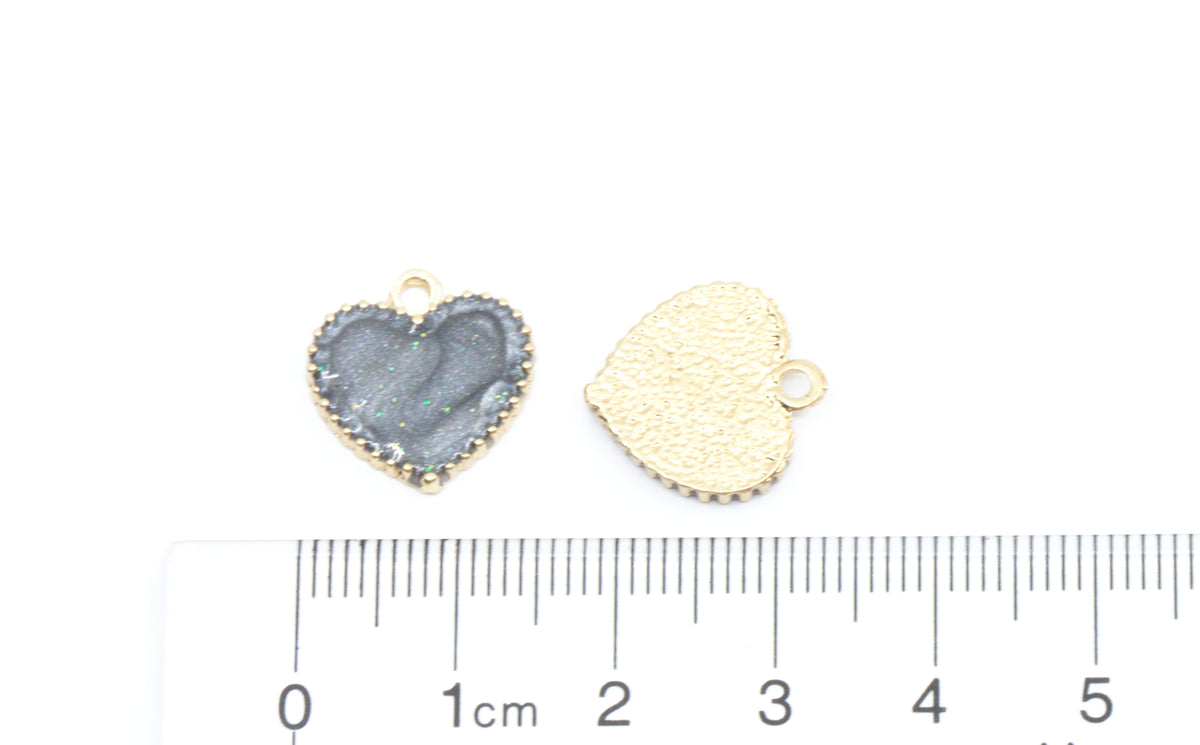 Two small heart-shaped jewelry charms shown on a white background with a ruler at the bottom for scale. 