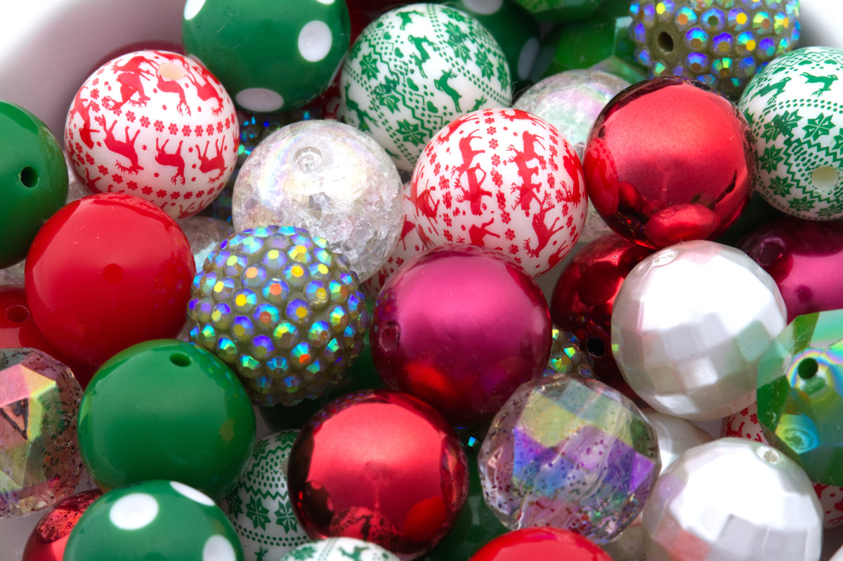 A close-up pile of colorful Christmas bubblegum beads, including shiny red, green, and white patterned, some iridescent glittery and faceted white beads