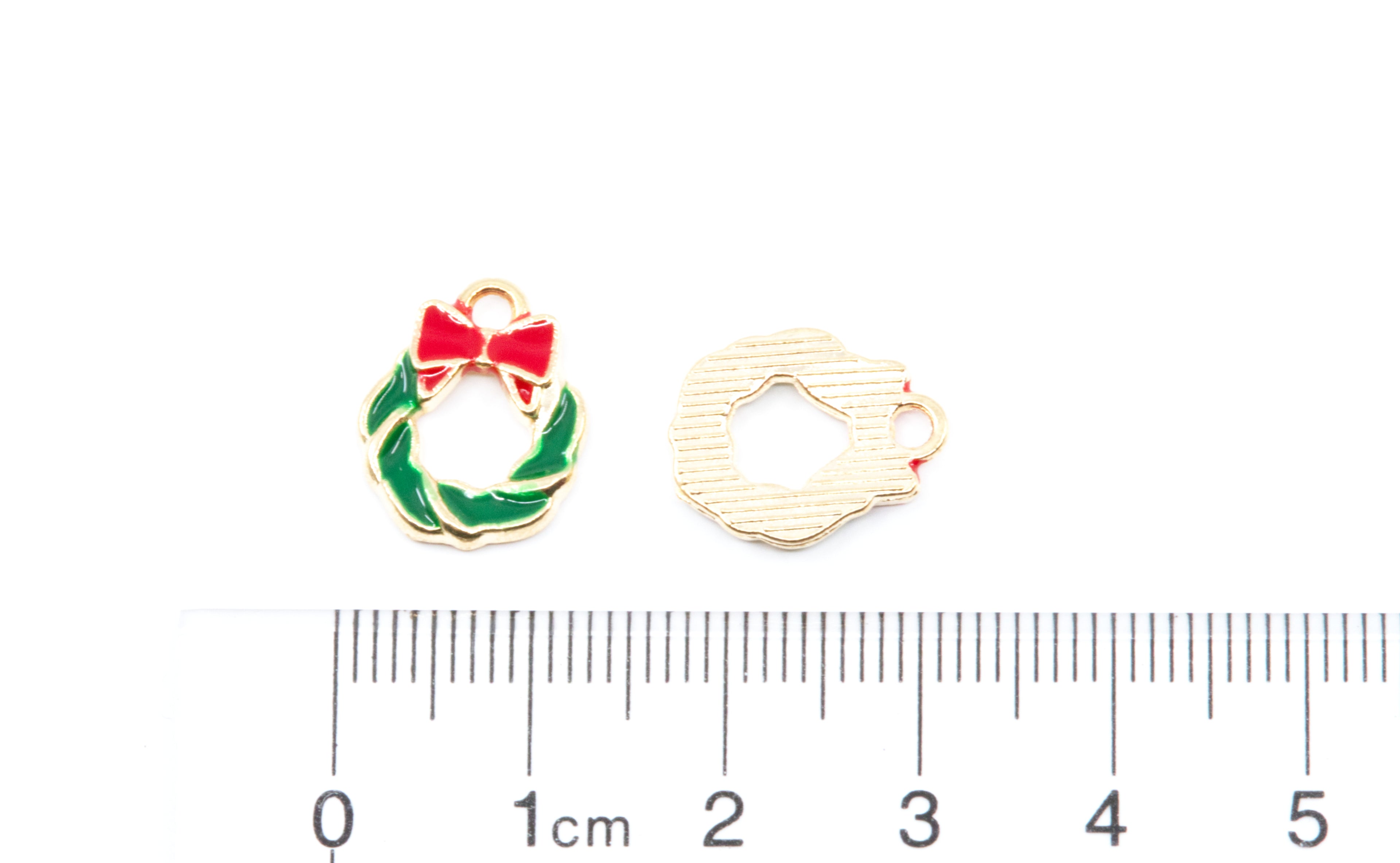 Two green Christmas wreath enamel charms shown on a white background above a ruler for scale