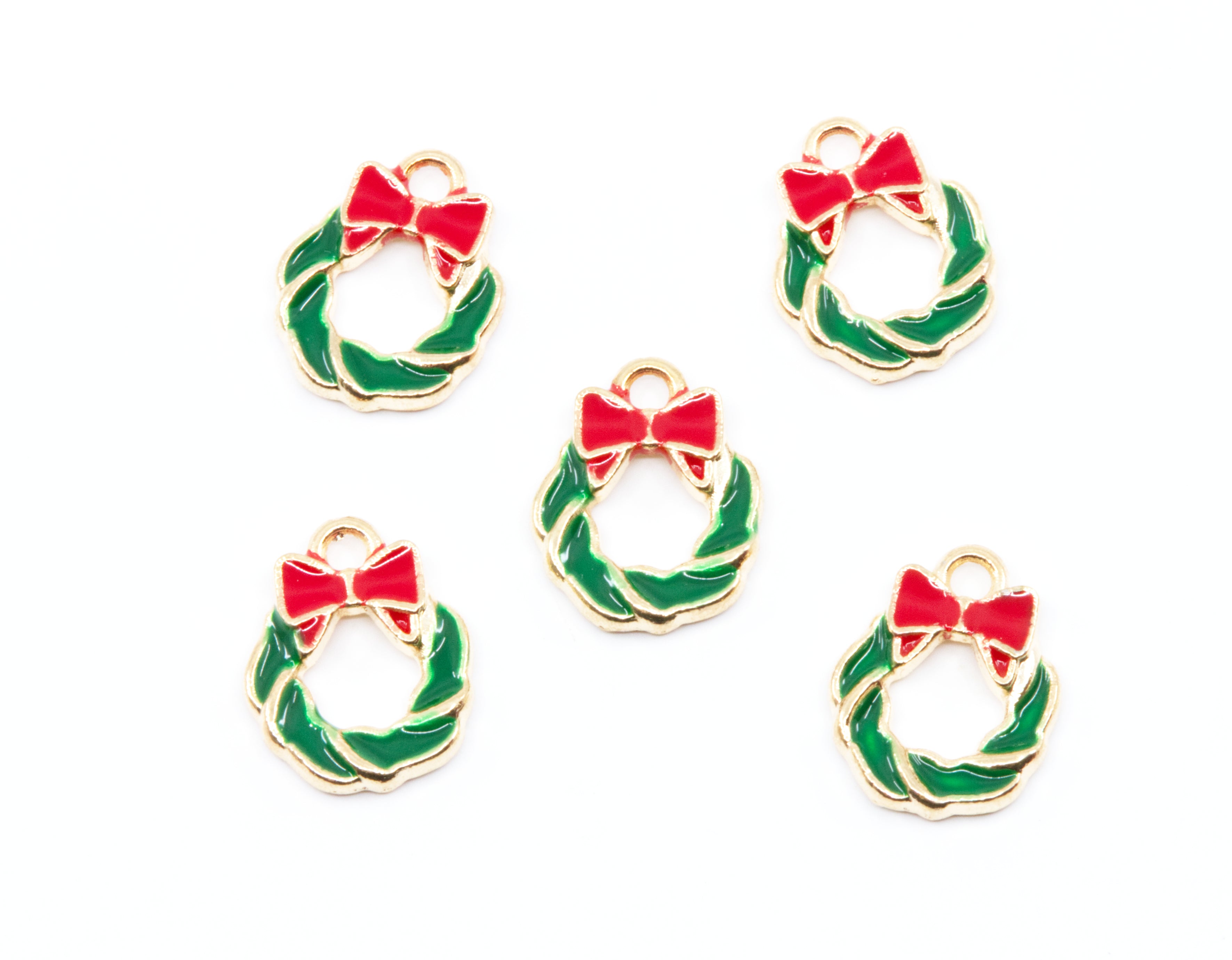 Five small holiday wreath charms with gold-tone metal edges, green enamel fill, and red bow details, arranged on a plain white background.