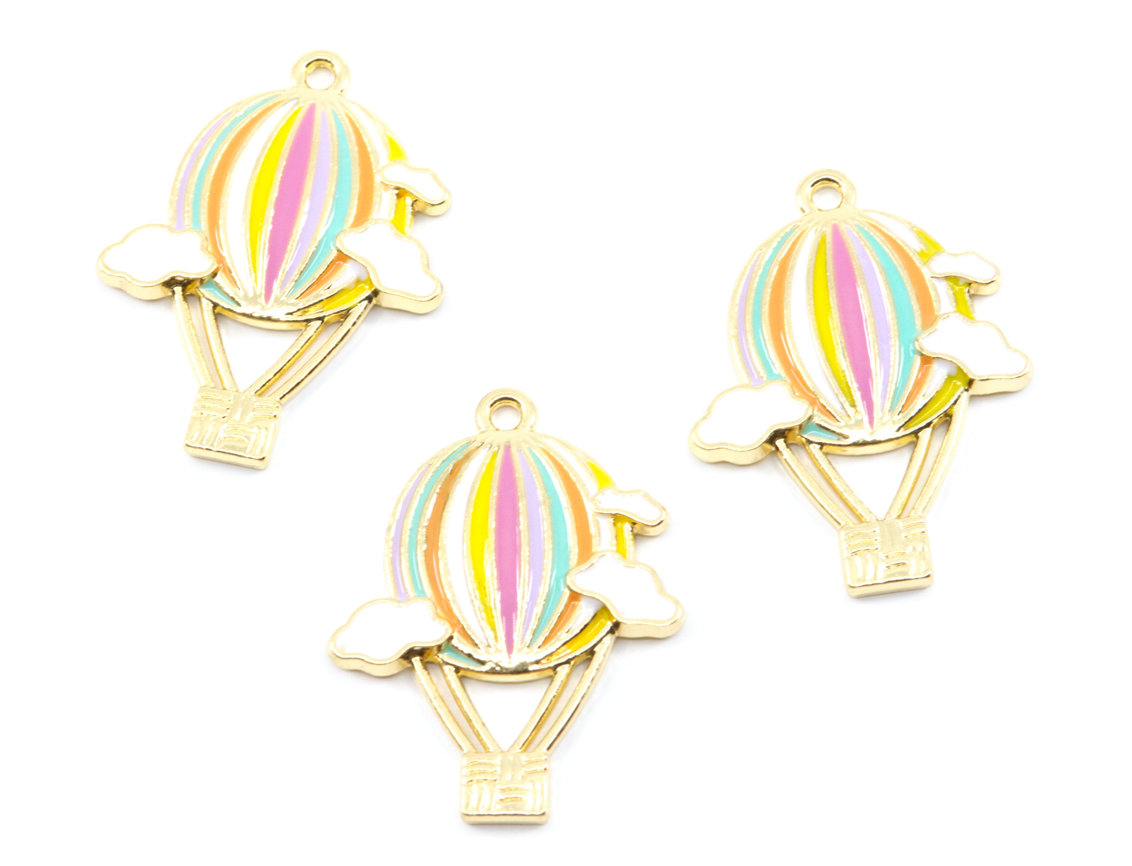 Three gold-plated hot air balloon charms with pastel rainbow stripes and small clouds, arranged on a plain white background.