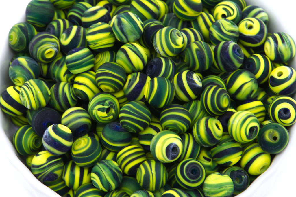 A close-up pile of round glass beads with swirls of black and yellow on a white background. 