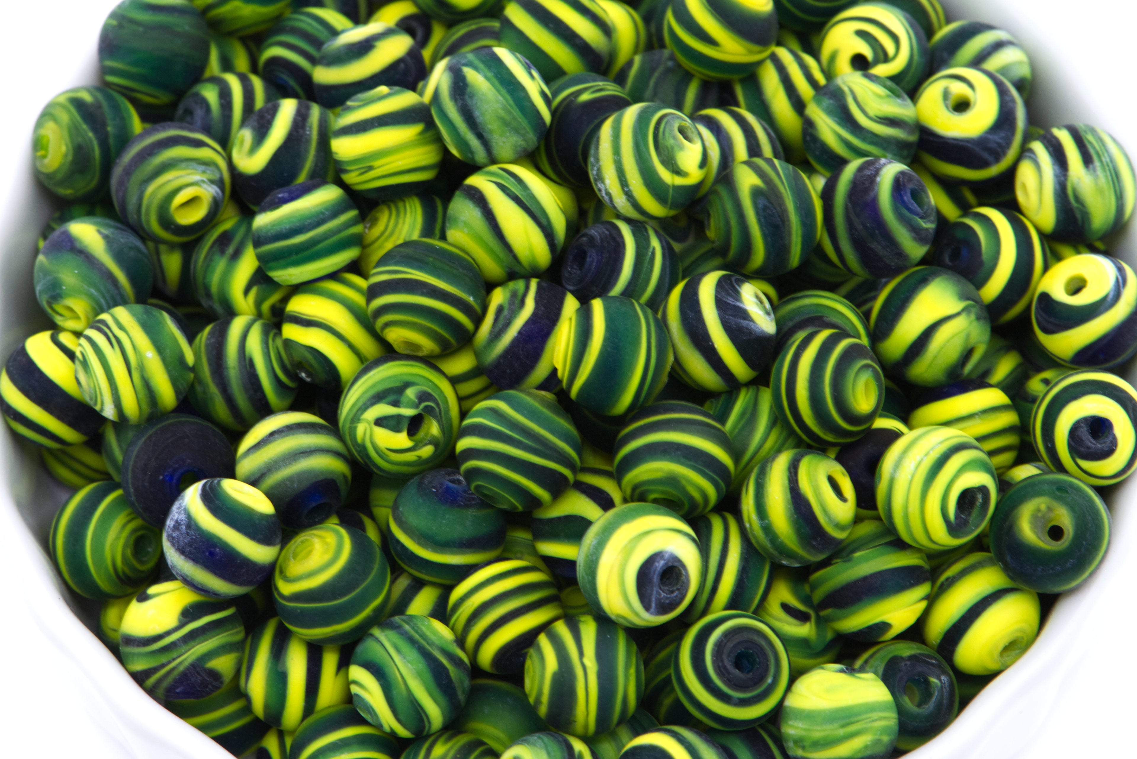 A close-up pile of round glass beads with swirls of black and yellow on a white background. 