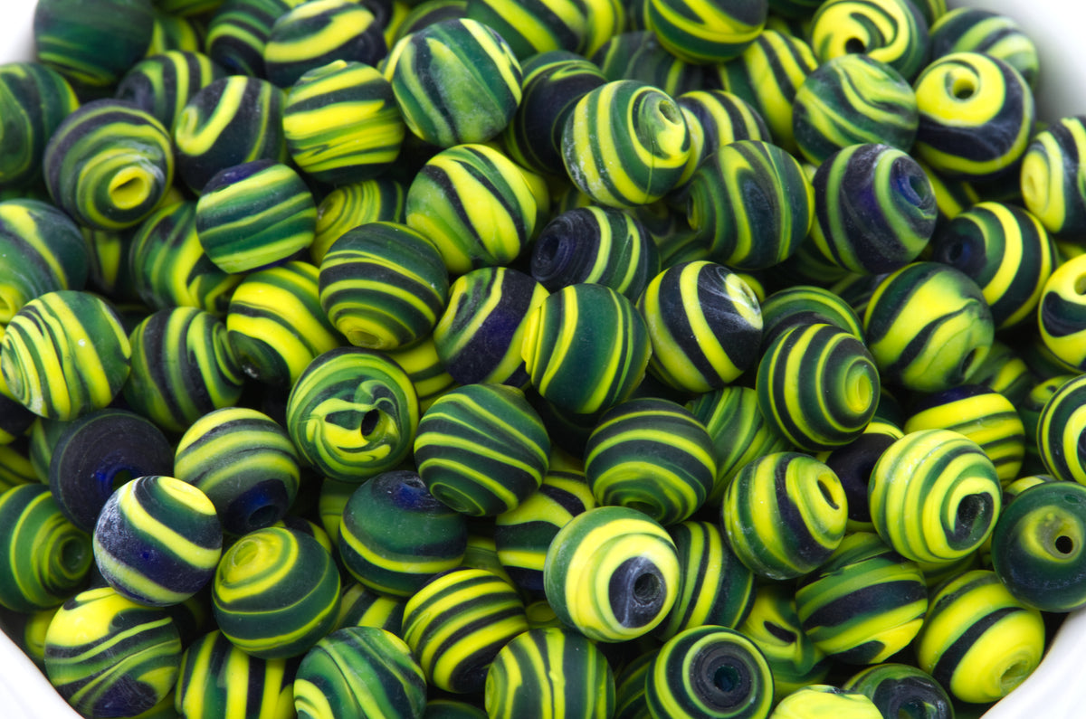 A close-up pile of round glass beads with swirls of black and yellow on a white background. 
