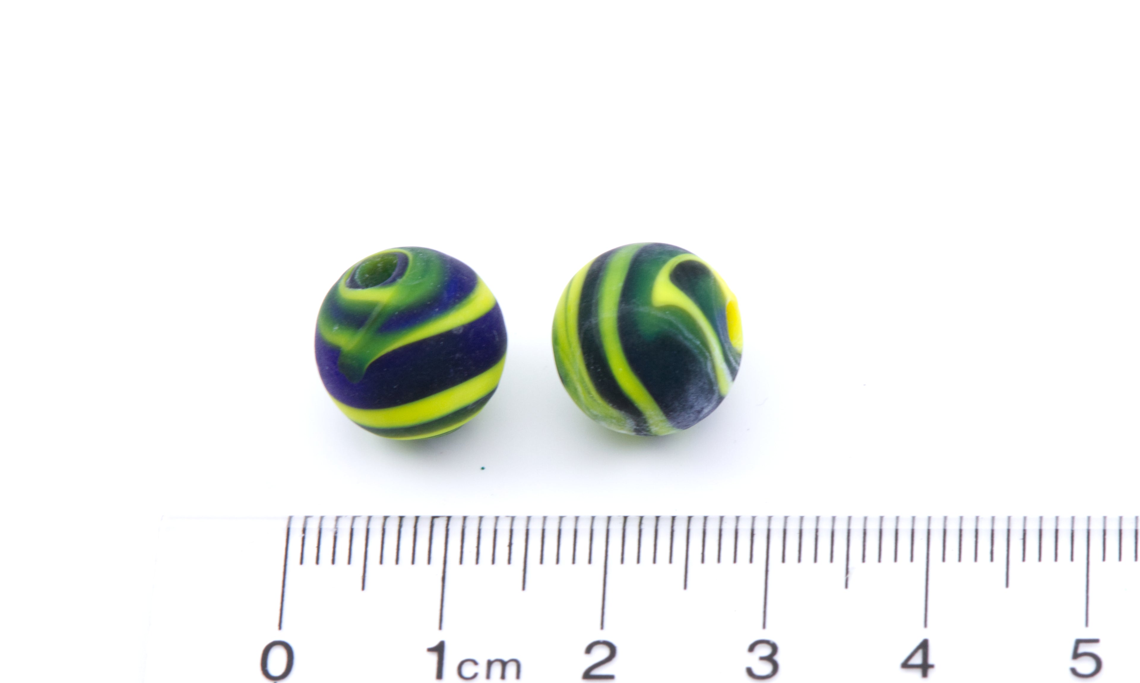 Two small round glass beads with black and yellow swirls shown next to a cm ruler on a white background.