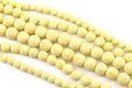 Multiple strands of pale yellow porous lava stone beads arranged diagonally on a clean white background.