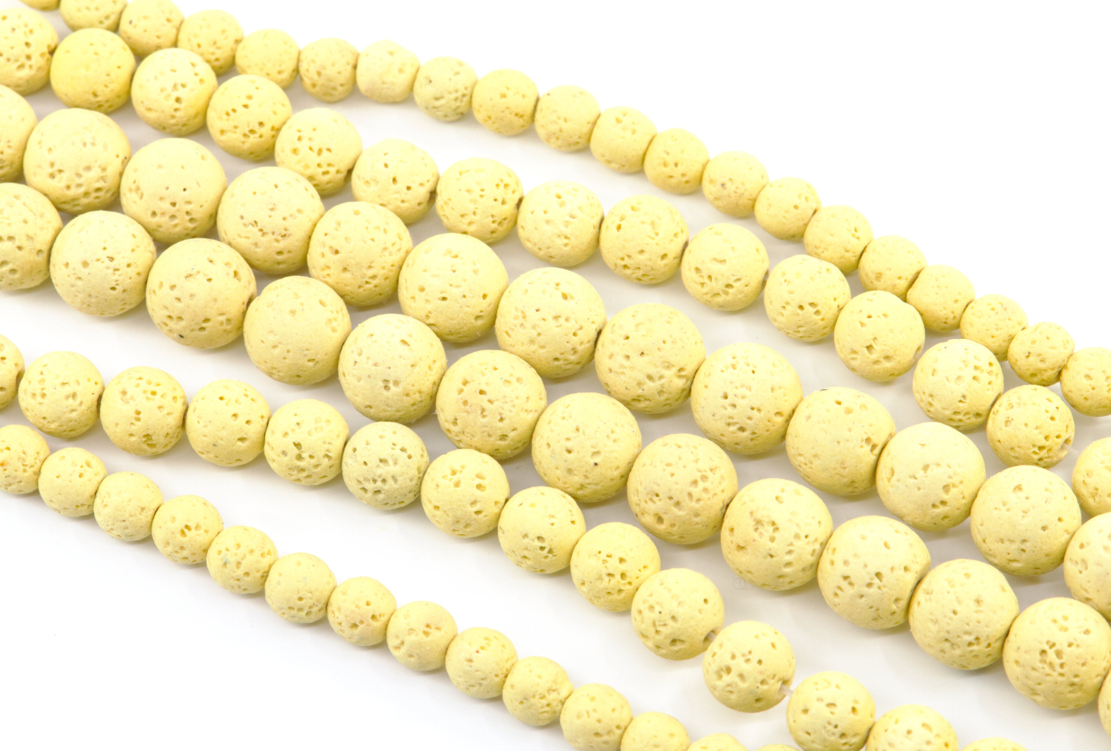 Multiple strands of pale yellow porous lava stone beads arranged diagonally on a clean white background.