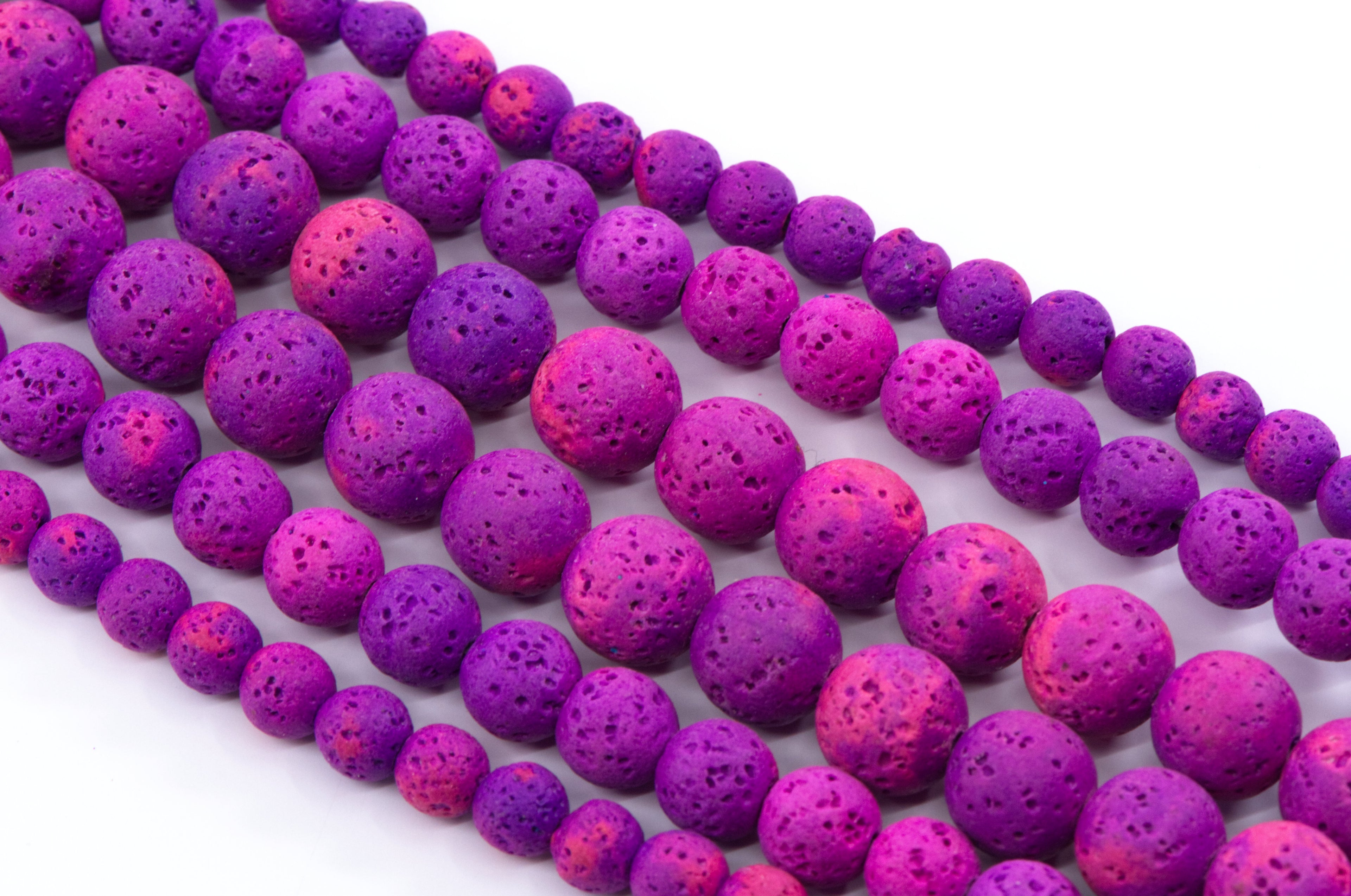 Multiple strands of porous lava stone beads in vibrant shades of purple and pink, arranged diagonally on a clean white background.
