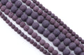 Multiple strands of porous purple lava stone beads in varying sizes, displayed diagonally on a clean white background.
