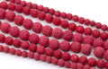 Red porous lava stone beads strung on strands, arranged diagonally on a white background.