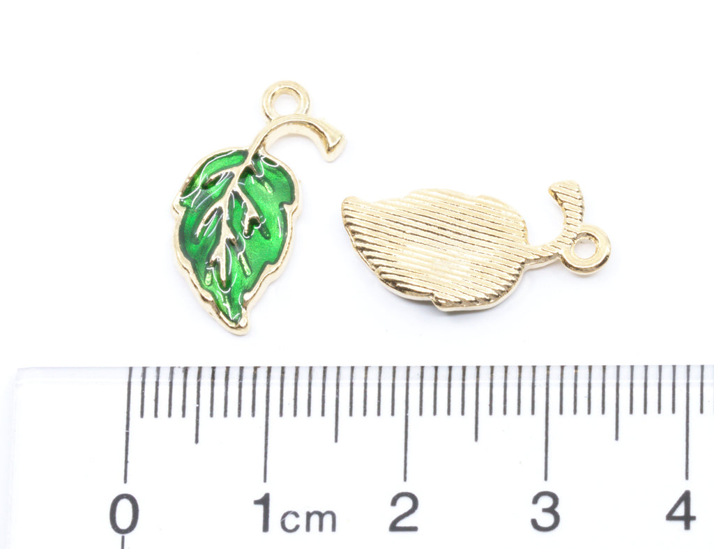 Two small leaf-shaped jewelry charms  on a white background with a ruler at the bottom for scale.